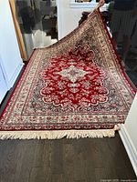 Full view of the Persian inspired Kirman Shah rug showing red central medallion and borders, fringed ends, and condition.