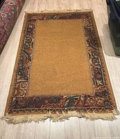 Full view of the Persian inspired rug showing the sand-colored central area with colorful borders and fringed edges.