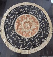 Round Persian inspired tablecloth laid flat showing tan central embroidered medallion on black background with gold swirling embroidery and gold fringe around edges.