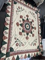 Full view of one side of the quilt laid out flat on the floor showing cream background with central floral medallion and applique details