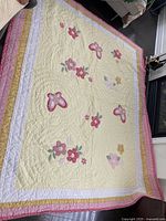 Full view of reversible quilt spread out on the floor showing yellow background with butterfly and floral appliqué designs and a multicolored border.
