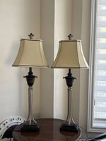 Photo showing the pair of two matching decorative table lamps placed on a dark wood table near a window.