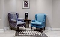 Two wingback chairs and a small round side table positioned in a corner of a room, showing the upholstery and details of each chair.