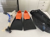 Swimming fins, snorkel mask and tube, and mesh bag laid out on a surface.