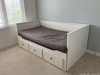 Full view of white daybed frame with dark grey fitted sheet and three storage drawers