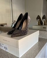 Pair of patterned Vince Camuto high heels on white shoe box, side angle, showing sleek pointed toe and gold stiletto heel.