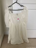 Front view of light cream summer dress hanging on hanger showing puffed sleeves and flowy skirt.