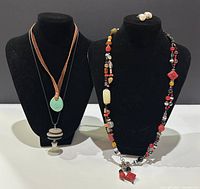 Two necklaces displayed on black busts, one with colorful beads and a pendant, the other with turquoise pendant and silver rings, plus pearl drop earrings on top