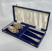Pair of vintage English silver plated serving spoons with embossed fruit in original blue case with satin lining, showing overall good condition and minor wear.