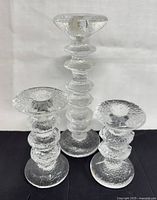 Front view of set of three clear textured Finnish IITTALA Festivo glass candle holders grouped on white and black background.