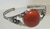 Front angle view showing the coral centerpiece and silver floral engravings on the cuff bracelet.