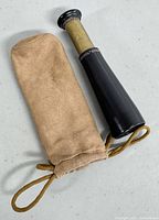 Monocular and tan suede pouch laid flat side by side on a table.