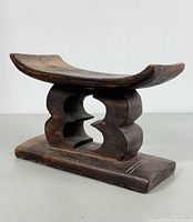 Front-angle view showing carved wooden stool with curved seat and geometric base details.
