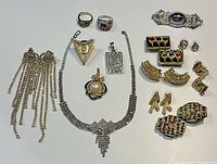 Overall costume jewelry lot laid out on a white surface, showing all pieces including rings, earrings, pendants, and choker necklace.