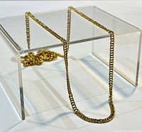 Gold chain necklace draped over clear stand showing length and chain style.