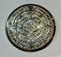 Front view of round silver brooch with raised Aztec calendar design with intricate details and central figure.