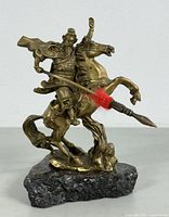 Front and side view of vintage brass Asian dragon warrior statue mounted on rough stone base, showing detailed armor, horse posture, and spear with red yarn wrapping.