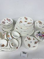 Wide view of the entire Coalport china set with stacked plates, bowls, cups, and saucers showing floral patterns and scalloped edges.