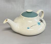 Side view of vintage Myott Safari Ironstone teapot showing off-white speckled body with black and blue starburst decorations and blue lid.