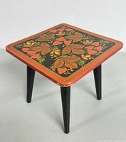 Front angled view showing detailed hand painted floral design on stool top and black tapered legs with minor wear