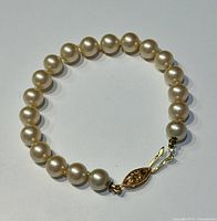 Full view of the pearl bracelet showing round pearls and the gold-tone decorative clasp.