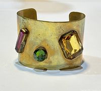 Photo of front of wide cuff bracelet showing rectangular purple, round green, and irregular yellow gemstones on brass or gold-toned metal