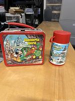 Photo of vintage Disneyland Wonderful World lunchbox and matching thermos on table with workshop background