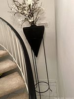 Full view of the 5-ft tall black metal vase with white artificial flowers near stairway and wall