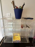 Clear acrylic organizer shelf with compartments, holding craft tools including scissors and pens