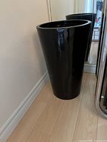 Tall black tapered plastic planter placed near corner wall and mirror, showing full height and shape.