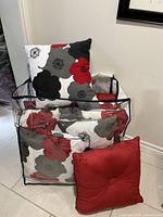 Nine cushions in floral and solid red cotton fabric with storage bag at base of wall near tiled floor