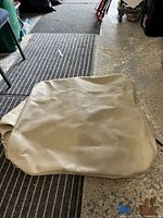 Folded synthetic beige air conditioner cover laid on garage floor, showing surface texture and condition.