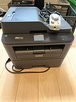 Front and top view of Brother MFC-L2710DW printer showing paper trays and control pad placed on top.