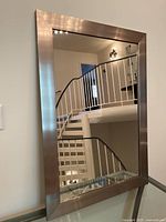 Front view of the rectangular mirror showing brushed metal frame and reflective surface, hung on wall near stairway.