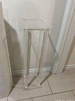 Full view of clear acrylic pedestal stand showing height and structure against a wall.