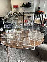 Wide view of several clear acrylic storage containers of varying sizes and styles arranged on a table in a garage setting.