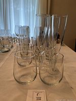 Various types of clear glassware including stemless glasses, champagne flutes, and tall tumblers arranged on table.