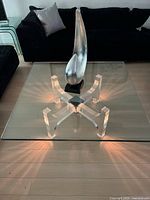 Full view of square glass coffee table with acrylic base and decorative accent on top, lit from under the base.