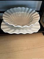 Stacked white ceramic serving dishes with fluted edges shown from above on a shelf.