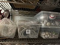 View of shelves with plastic containers holding various craft supplies including ribbons, decorative stones, and ornaments.