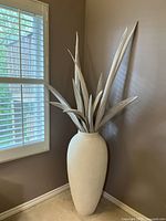 Full view of the tall cream plaster vase with dried palm leaves in corner near window.