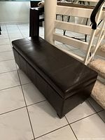 Closed view of the dark brown faux leather storage ottoman showing tufted top and rectangular shape.