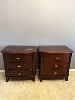 Two side-by-side dark brown wooden nightstands with three drawers each, minor surface scratches on top of one shown.