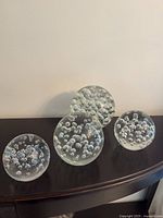 Four clear glass paperweights displayed on a dark wood surface, showing their bubble-filled interiors.