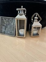 Two metal lanterns with glass panels and rope handles alongside a decorative wooden tray with circular pattern under glass.