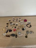 View of over 30 assorted souvenir keychains laid out on a wooden surface showing various designs and themes including hearts, logos, and travel-related icons.