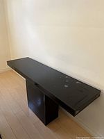 Full front view of the black acrylic console table placed against a wall, showing the rectangular shape and glossy surface with some chips.