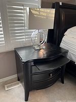 Front and side view of one nightstand showing curved drawer fronts, espresso finish, slide-out tray and acrylic lamp on top