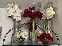 Front view of the holiday silk flower arrangements in glass vases with red and white flowers, silver pinecones, and glitter accents on a metal shelf.