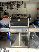 Front view of the Weber Genesis grill showing lid, cabinet doors, and side tables